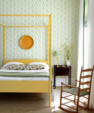 Bright bedroom with botanical green wallpaper, vibrant yellow four poster bed and accessories, wooden rocking chair