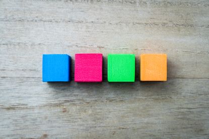 four wooden blocks -- one blue, pink, green and orange -- lined up with wooden background
