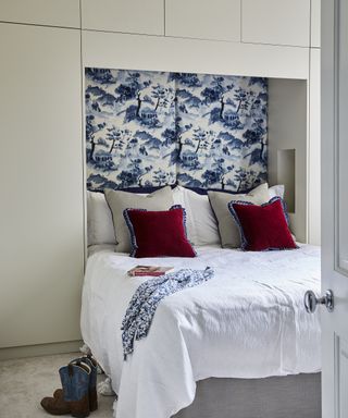 A white bed with a blue and white floral headboard and red cushions