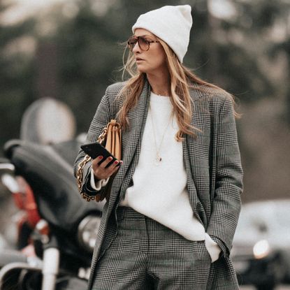 fashion week attendee wearing white beanie hat, checkered coat, sunglasses, and white sweater