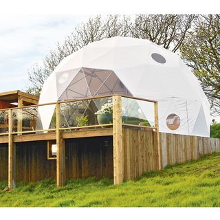 geo dome house with wooden base on green hill