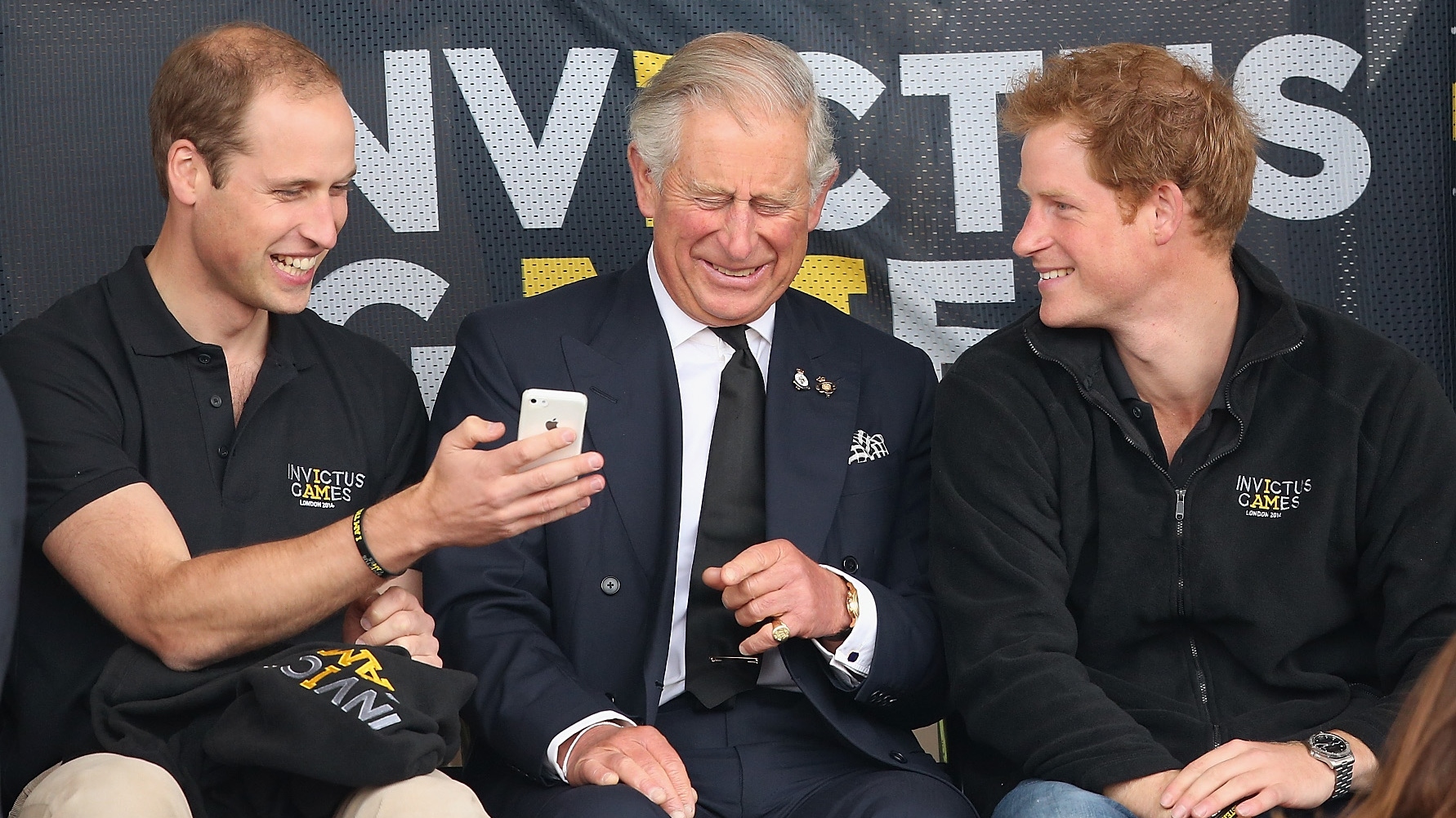 Prince William, Prince Harry and King Charles look at a mobile phone as they watch the athletics at Lee Valley Track during the Invictus Games on September 11, 2014