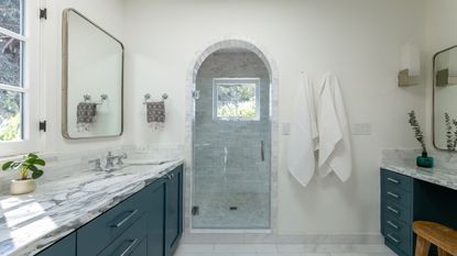 A white bathroom with dark blue vanities and marble countertops