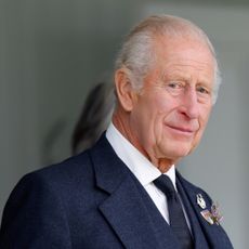 King Charles wearing a blue suit holding a walking stick