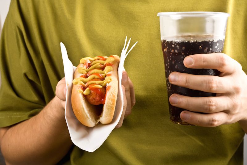 A man holds a soda and a hotdog