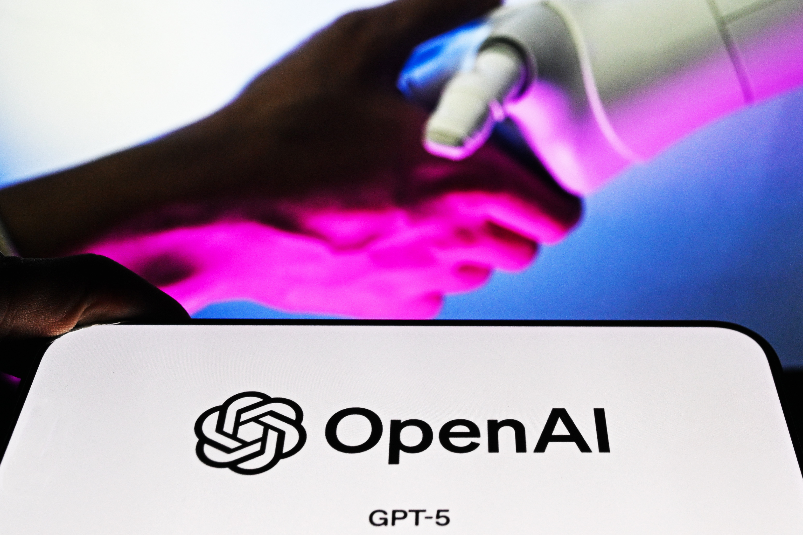 ANKARA, TURKIYE - AUGUST 13: In this photo illustration, the logo of OpenAI logo is being displayed on a mobile phone screen in front of another screen displaying a robotic hand, in Ankara, Turkiye on August 13, 2025. (Photo by Ismail Aslandag/Anadolu via Getty Images)