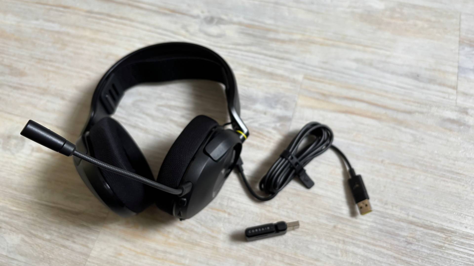 contents of the Corsair HS35 v3 headset box including the headset, mic, dongle, and USB C cable against a white hardwood floor background