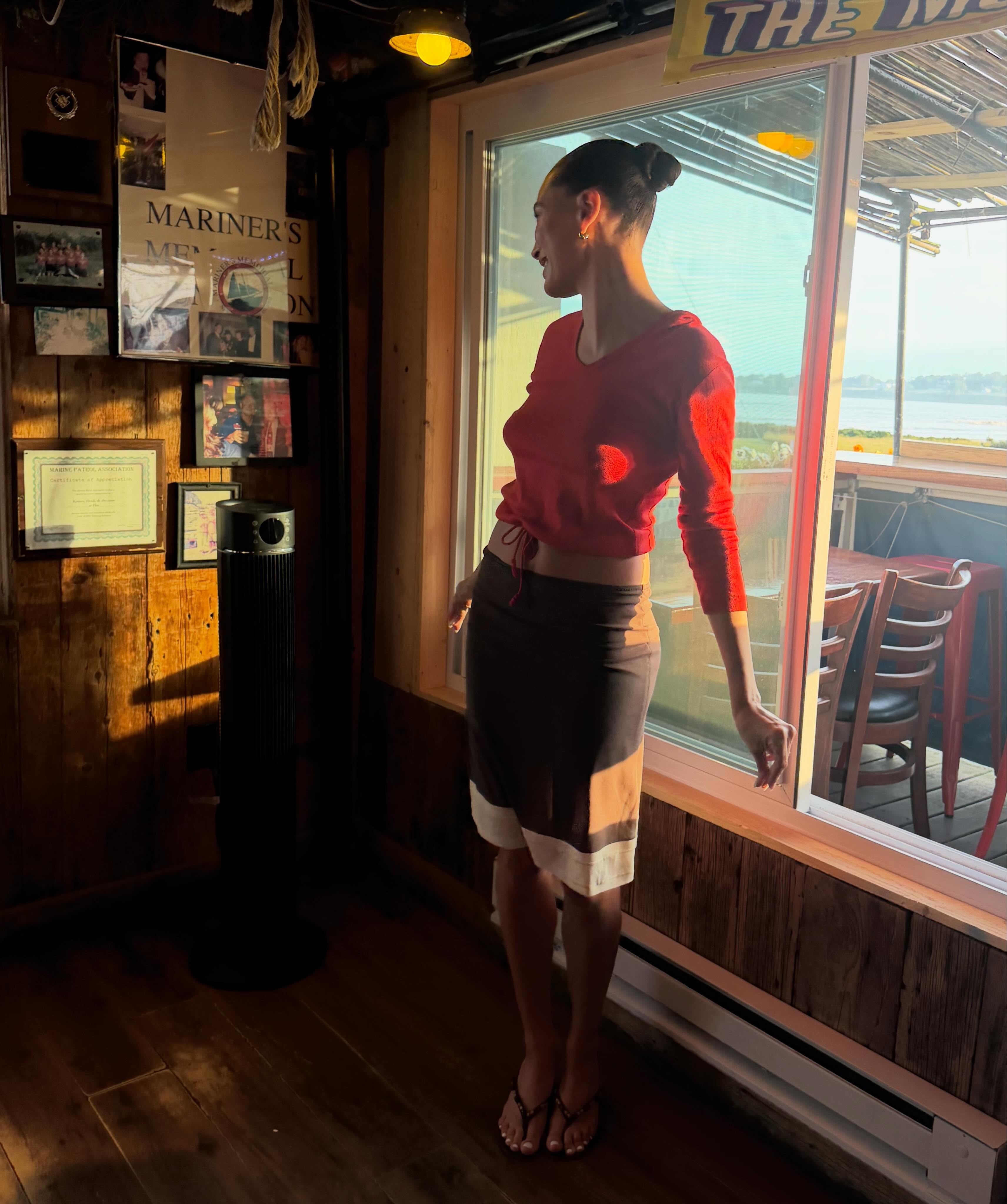 Hailey Bieber wearing a red sweater with a brown and white skirt and thong sandals.