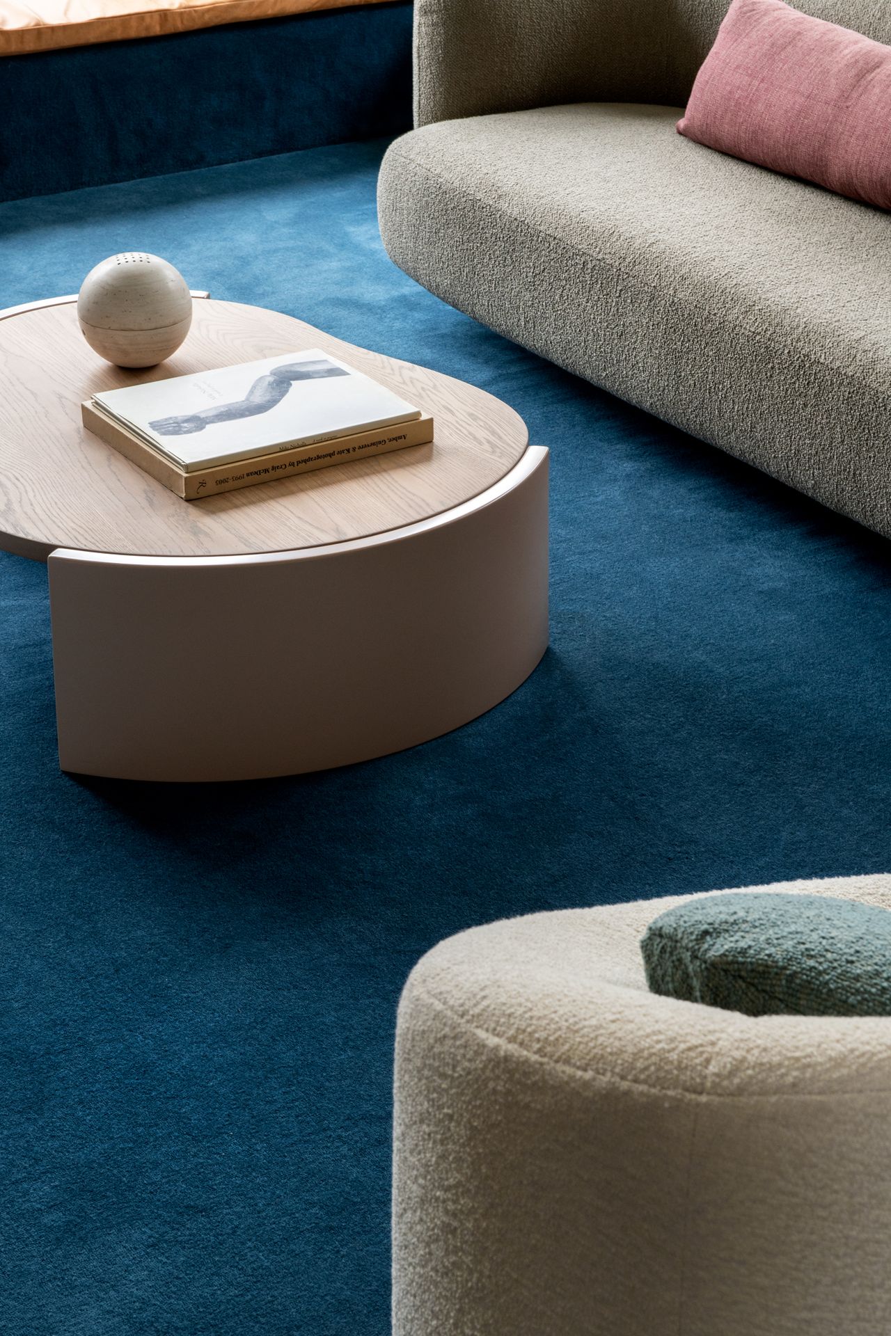 close up of living room floor covered in bright blue carpet, with timber coffee table, boucle armchair, and sofa