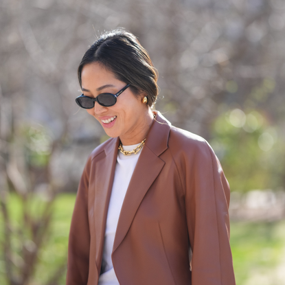 Korean SPF K-Beauty SPF Aimee Song wears black sunglasses, gold earrings, white t-shirt, shiny dark brown leather blazer jacket, outside Herm&egrave;s, during the Paris Fashion week