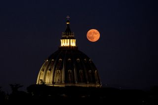 a large dome structure in the center with a big orange full moon shining just to the right of the dome.