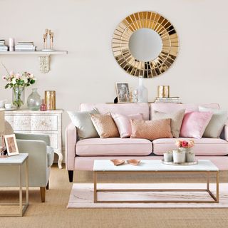 A neutral living room with a pink sofa and gold round mirror