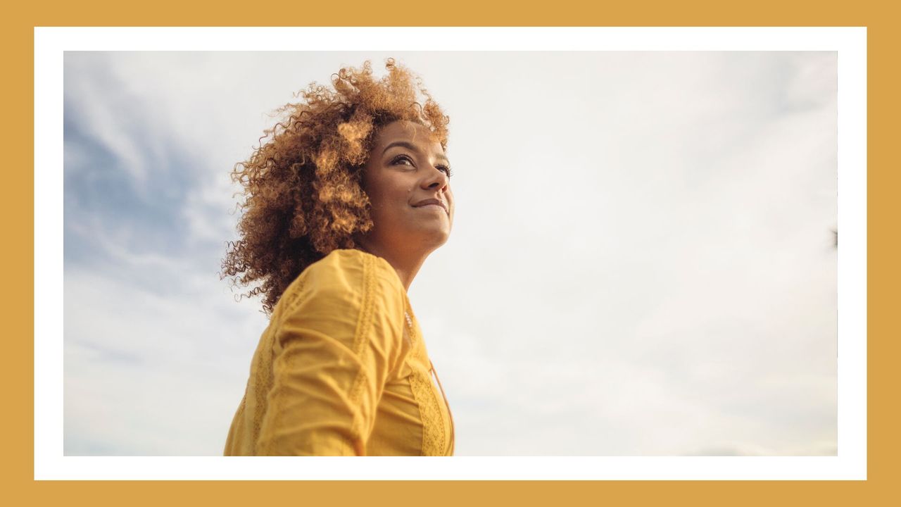 woman outside in a yellow shirt looking positive with camera angled towards the sky