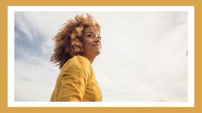 woman outside in a yellow shirt looking positive with camera angled towards the sky