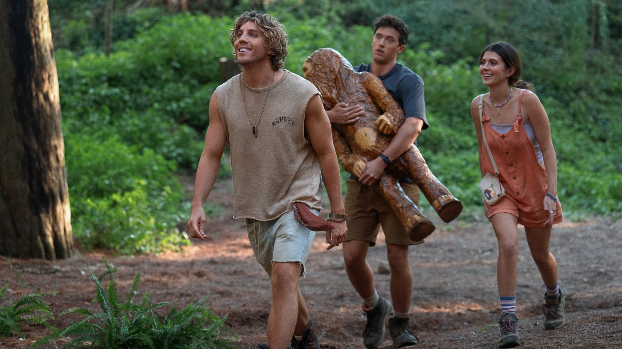 From left to right: Buck walking and smiling, Alex following him wide-eyed while carrying a large Big Foot state and Poppy walking next ot Alex and smiling.