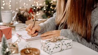Woman writing on a pad of paper next to a Christmas tree