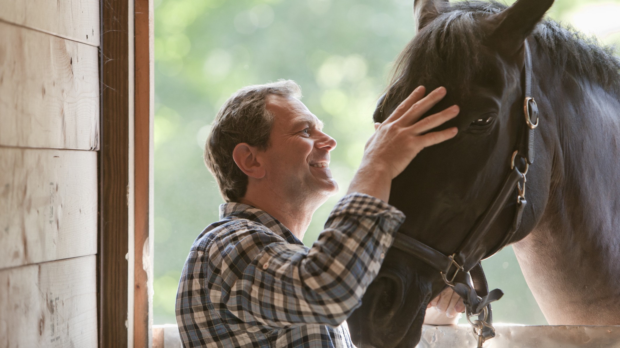 A smiling man in his forties pets a bridled horse.