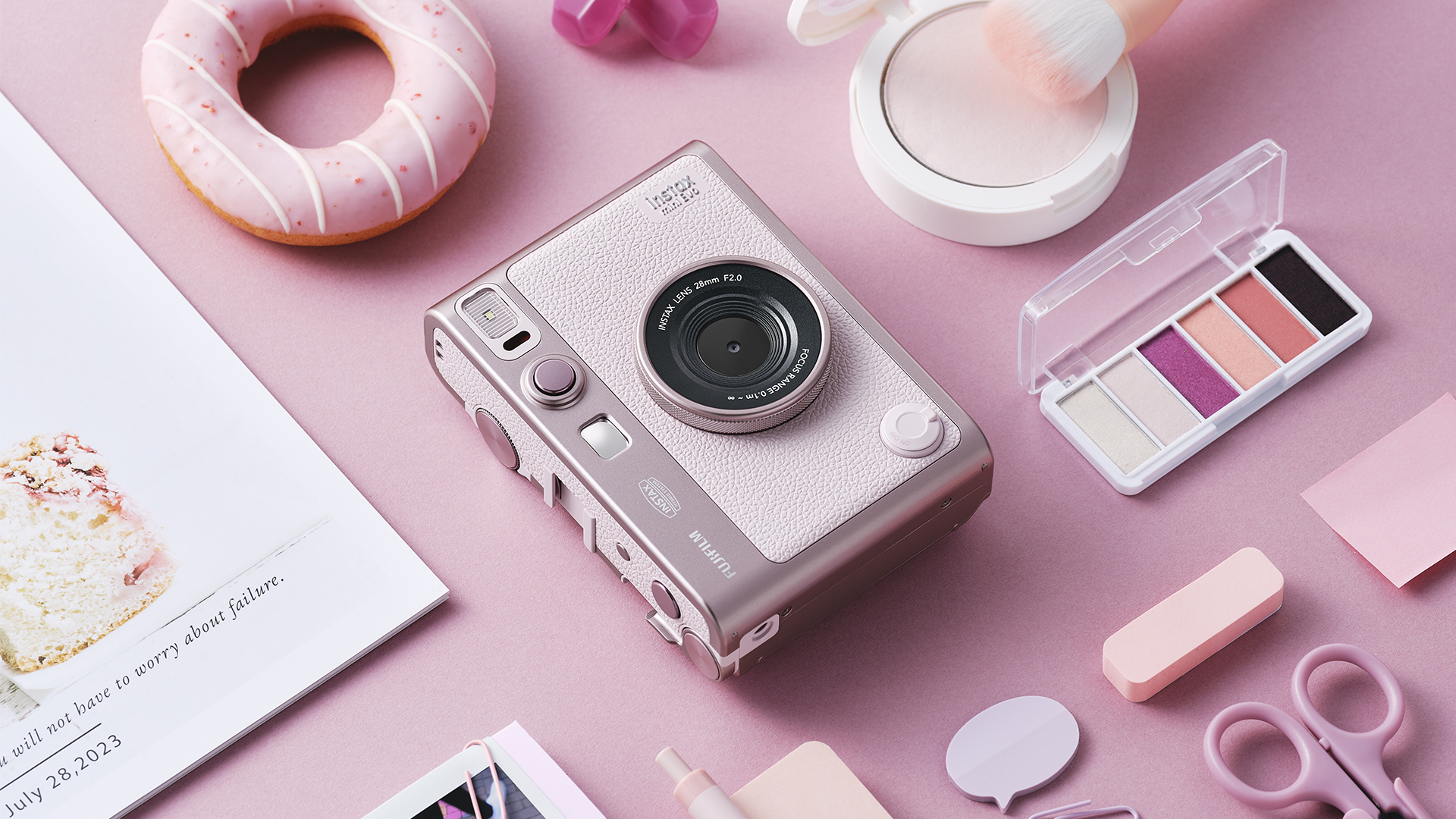 Fujifilm Instax Mini Evo Gentle Rose instant camera on a pink table surrounded by cosmetic items