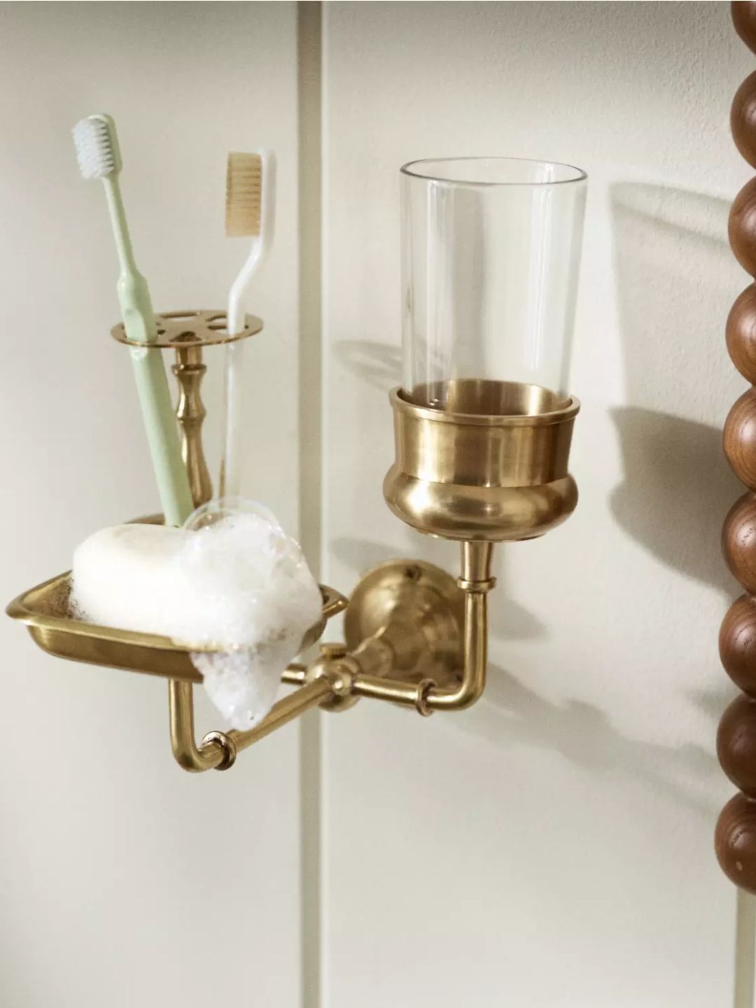 A brass bathroom organizer from Anthropologie with a toothbrush holder, a glass, and a soap tray