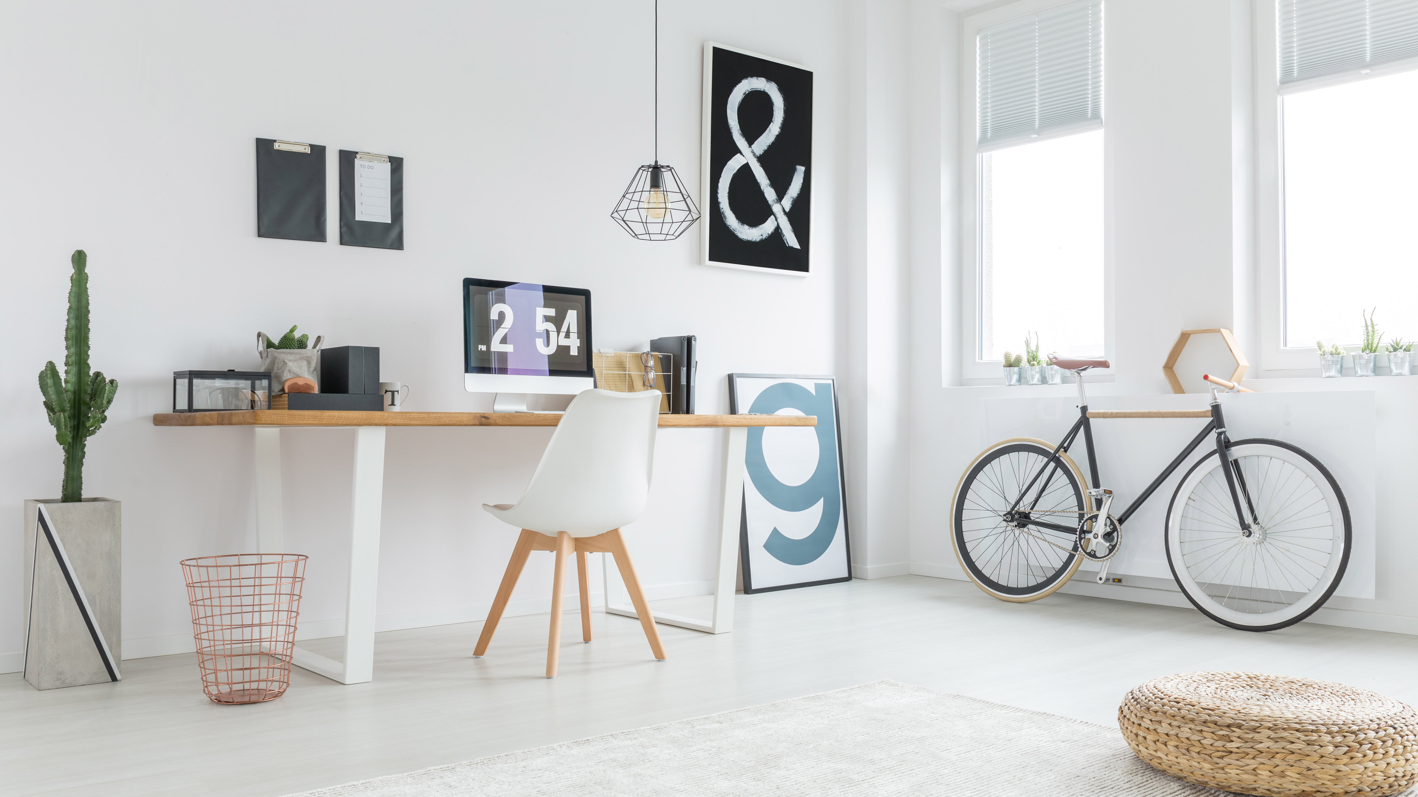 A home office which is painted white with a cactus and bicycle next to the desk