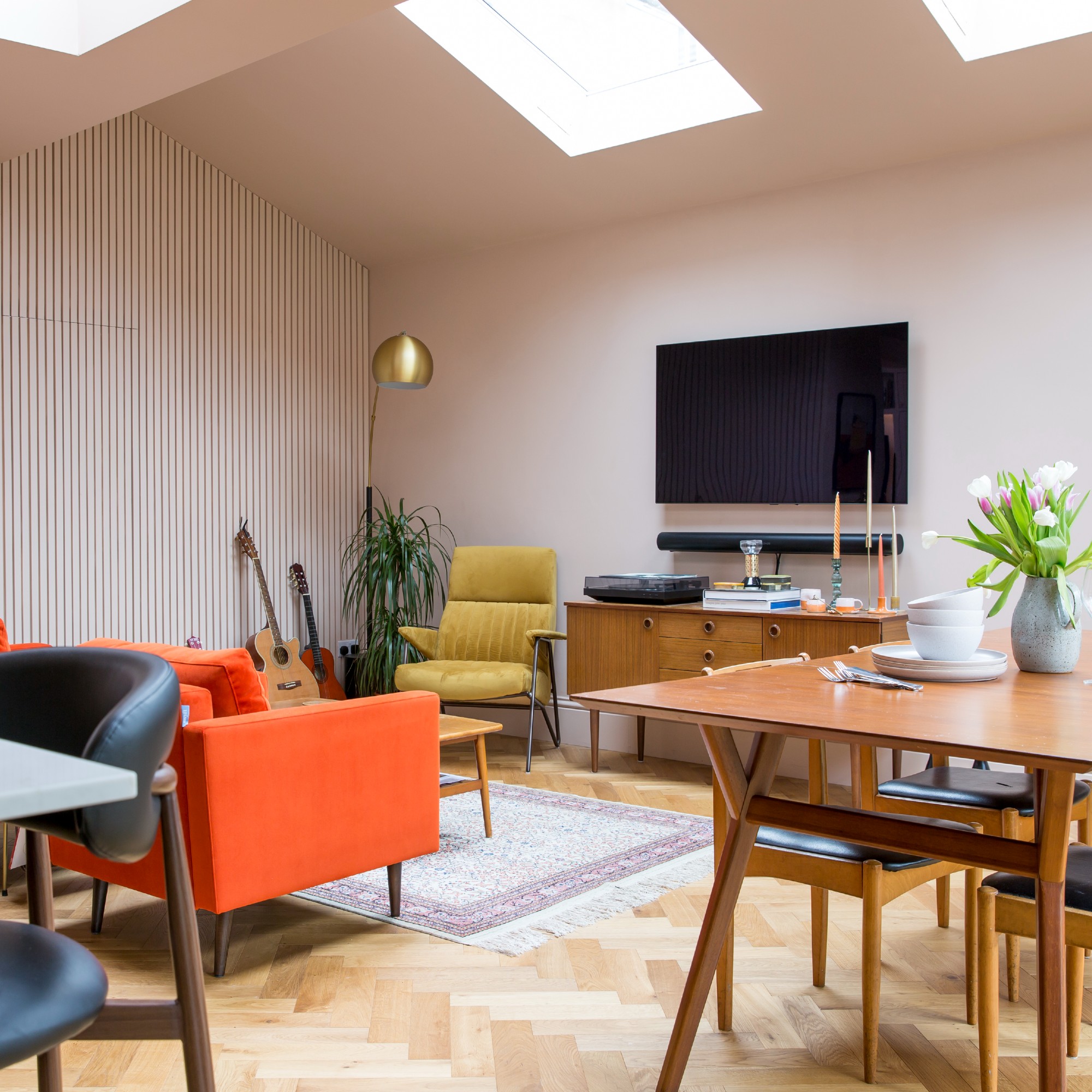 A living room with two orange armchairs and one yellow and a wall-mounted TV above a midcentury sideboard
