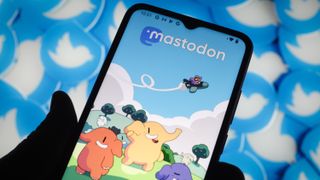 The Mastodon drawing with illustrations on a phone screen in front of a wall of Twitter logos to demonstrate Twitter vs Mastodon