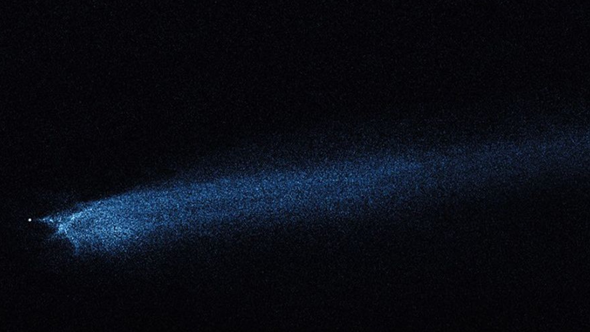 space telescope photo showing a long, dusty bluish tail extending from a bright white dot