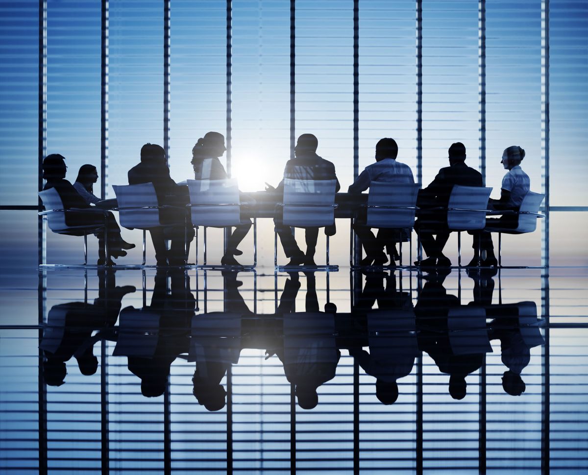 Colleagues sitting around a table in a boardroom before a window overlooking the city