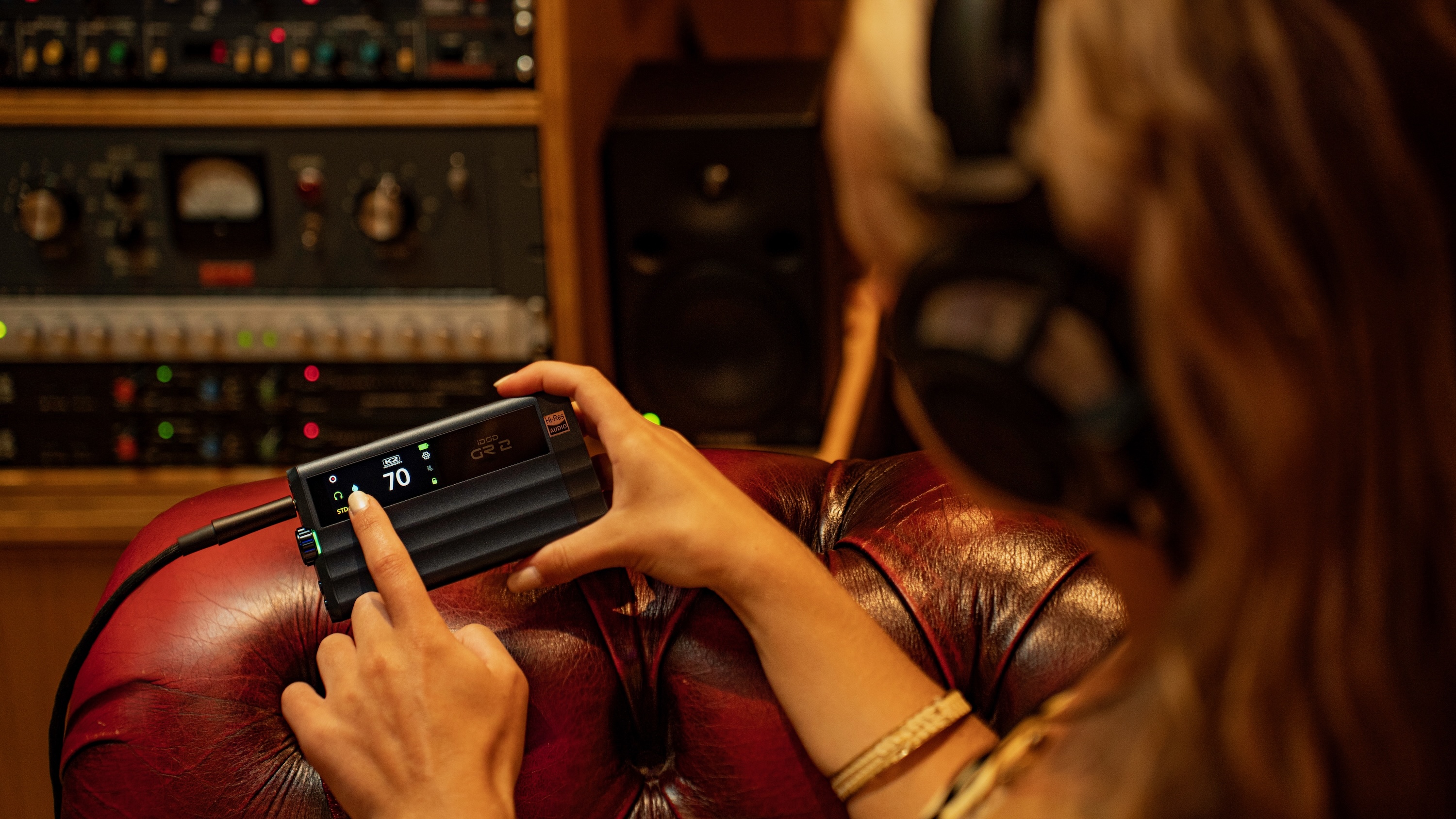 The iFi iDSD GR 2 being held by a woman wearing headphones on a red leather sofa.