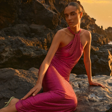 Model wearing a sequined halterneck dress sold at Karen Millen sat leaning on a rock