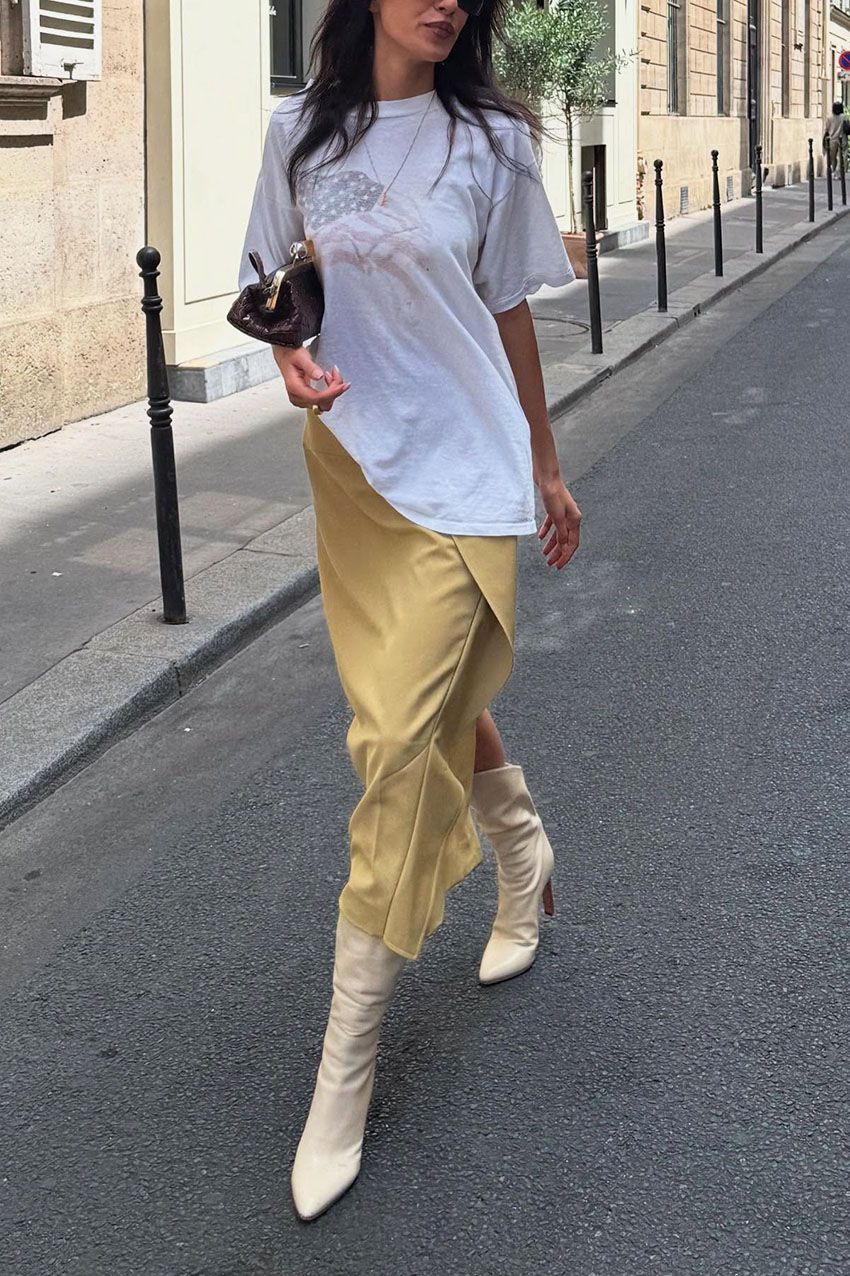 A woman wearing an oversized white t-shirt, yellow skirt, and white leather boots