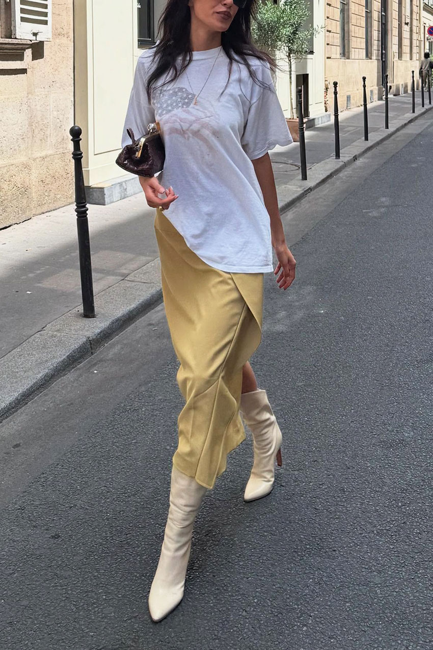 A woman wearing an oversized white t-shirt, yellow skirt, and white leather boots