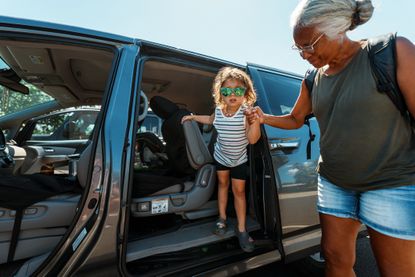 An active and healthy senior woman affectionately holds her three year old granddaughter's hand as the child climbs out of the passenger door of a mini van.