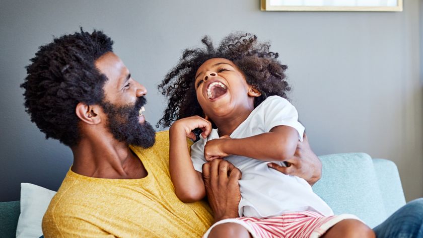 Shot of a cheerful young man holding his son and ticking him while being seated on a couch at home.