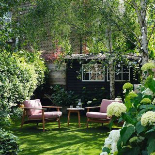Seating area in the garden surrounded by trees and flowerbeds with white and green hydrangeas