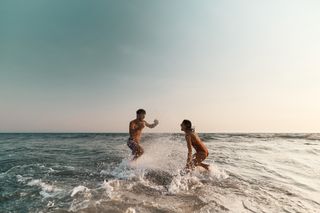 A happy couple having fun splashing each other in the sea.