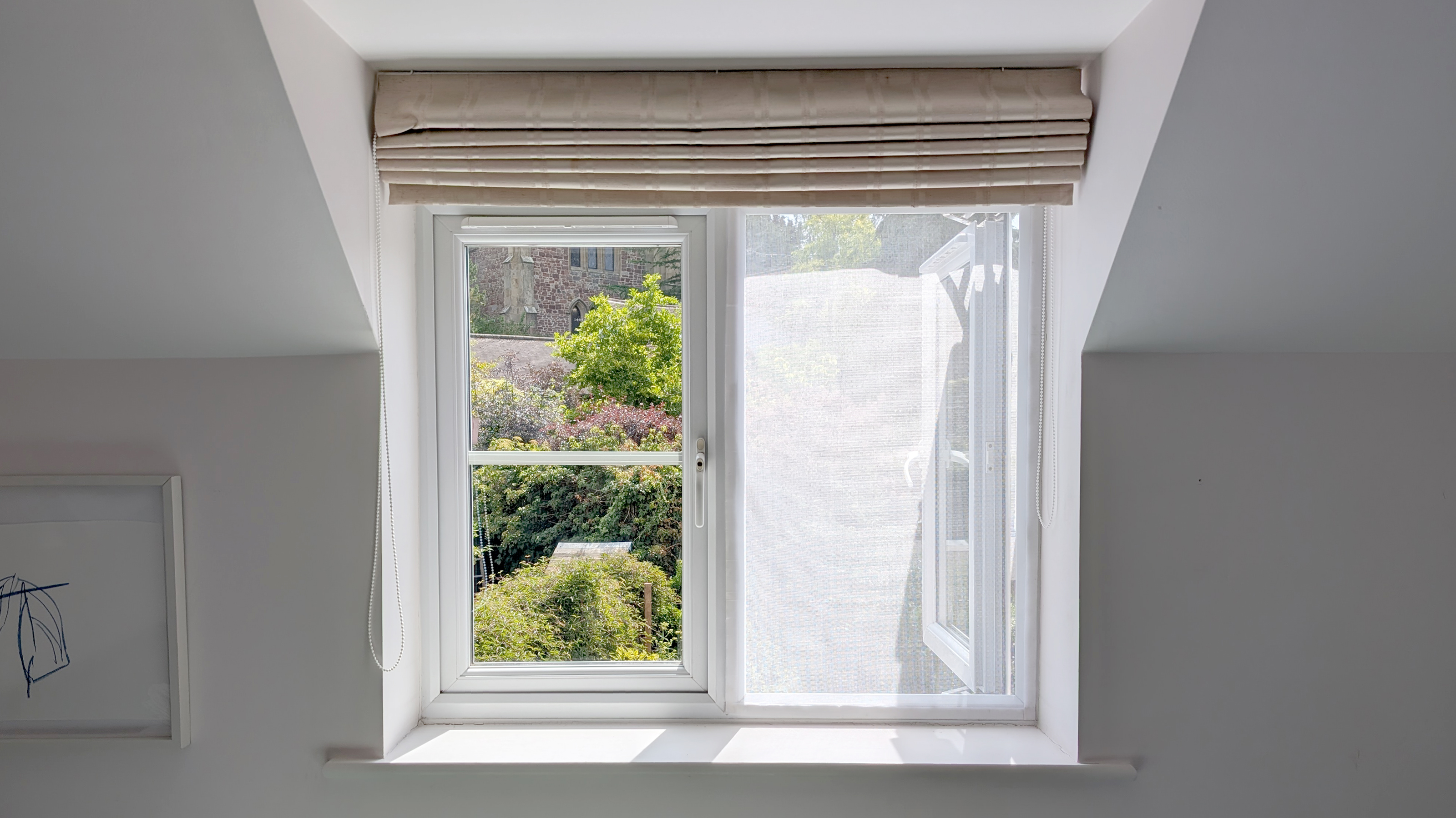 A DIY mosquito screen placed over a window in a bedroom with white walls