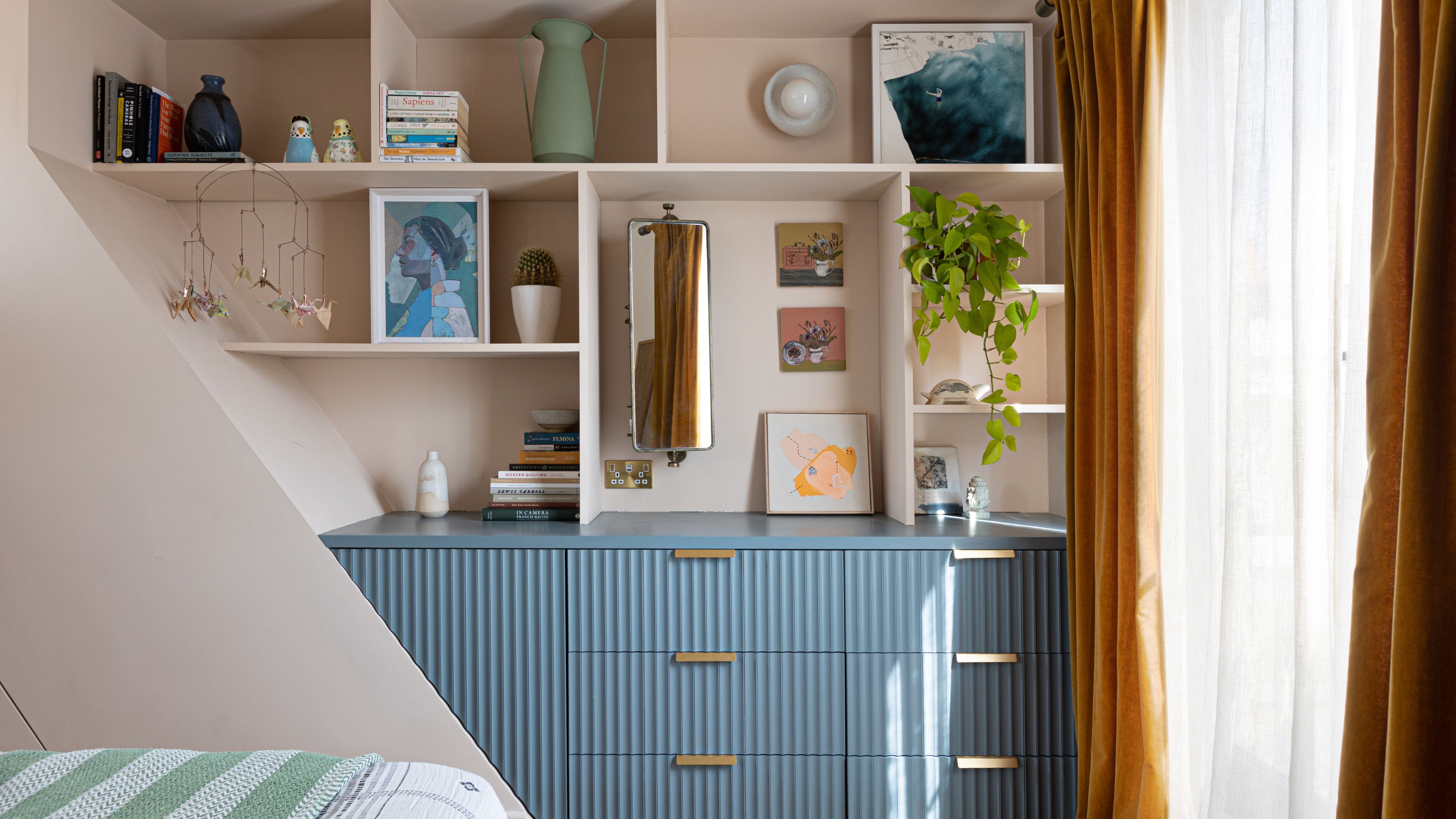 Bedroom wall with blue chest of drawers below lots of shelving 