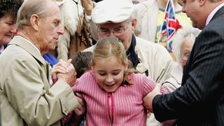 Prince Philip, Duke of Edinburgh helps a young girl over the barrier in order to give the Queen some flowers as she greets crowds on her 80th Birthday on April 21, 2006 in Windsor, England. Queen Elizabeth II celebrated her 80th birthday by meeting well wishers in the roads surrounding Windsor Castle