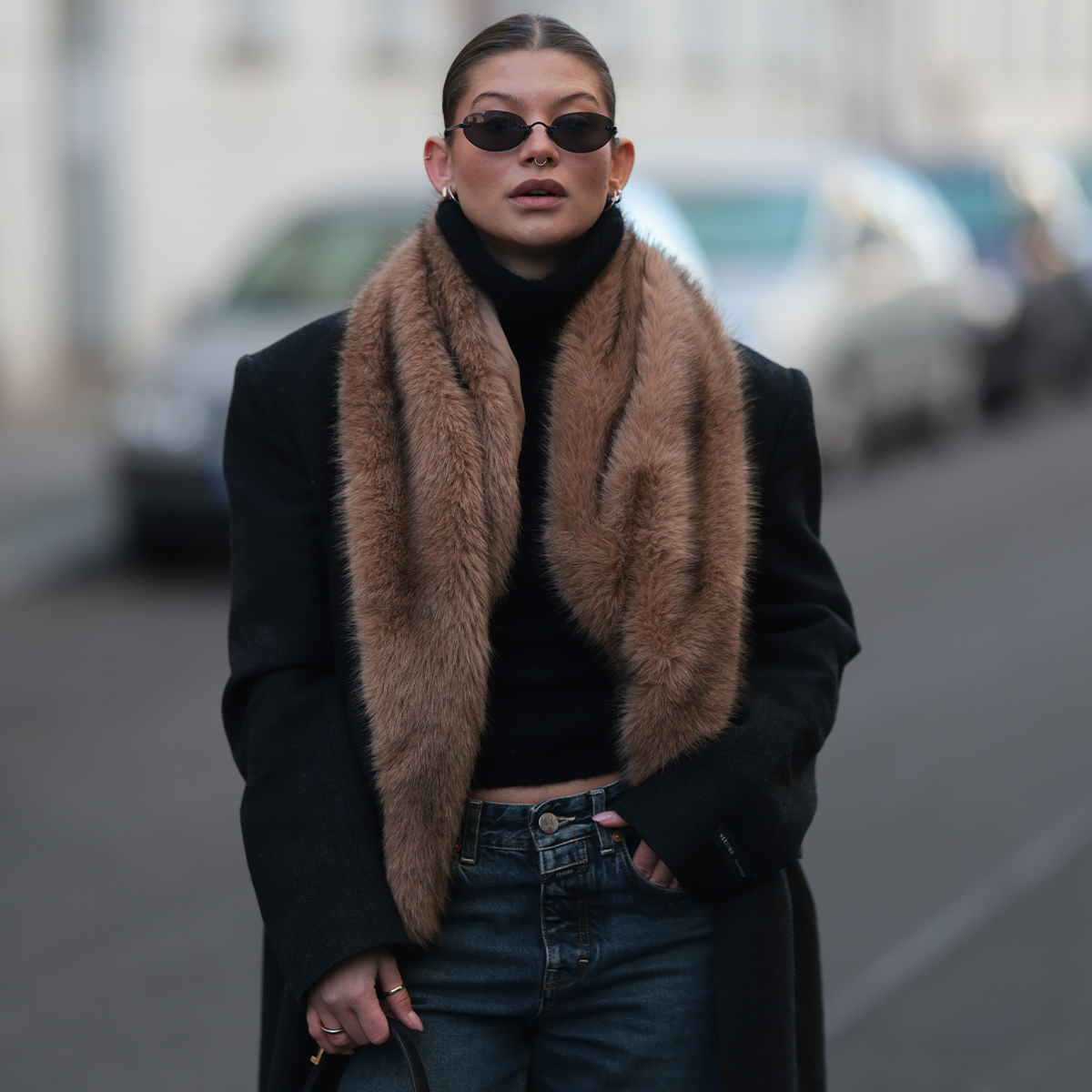 Woman in fur-trimmed coat, jeans, and sunglasses. 