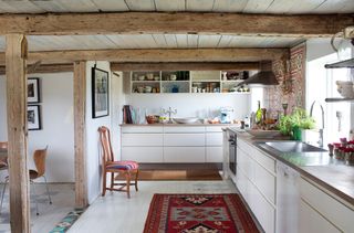 white glossy scandi kitchen with red rug on the floor and exposed beamed ceilling and supports