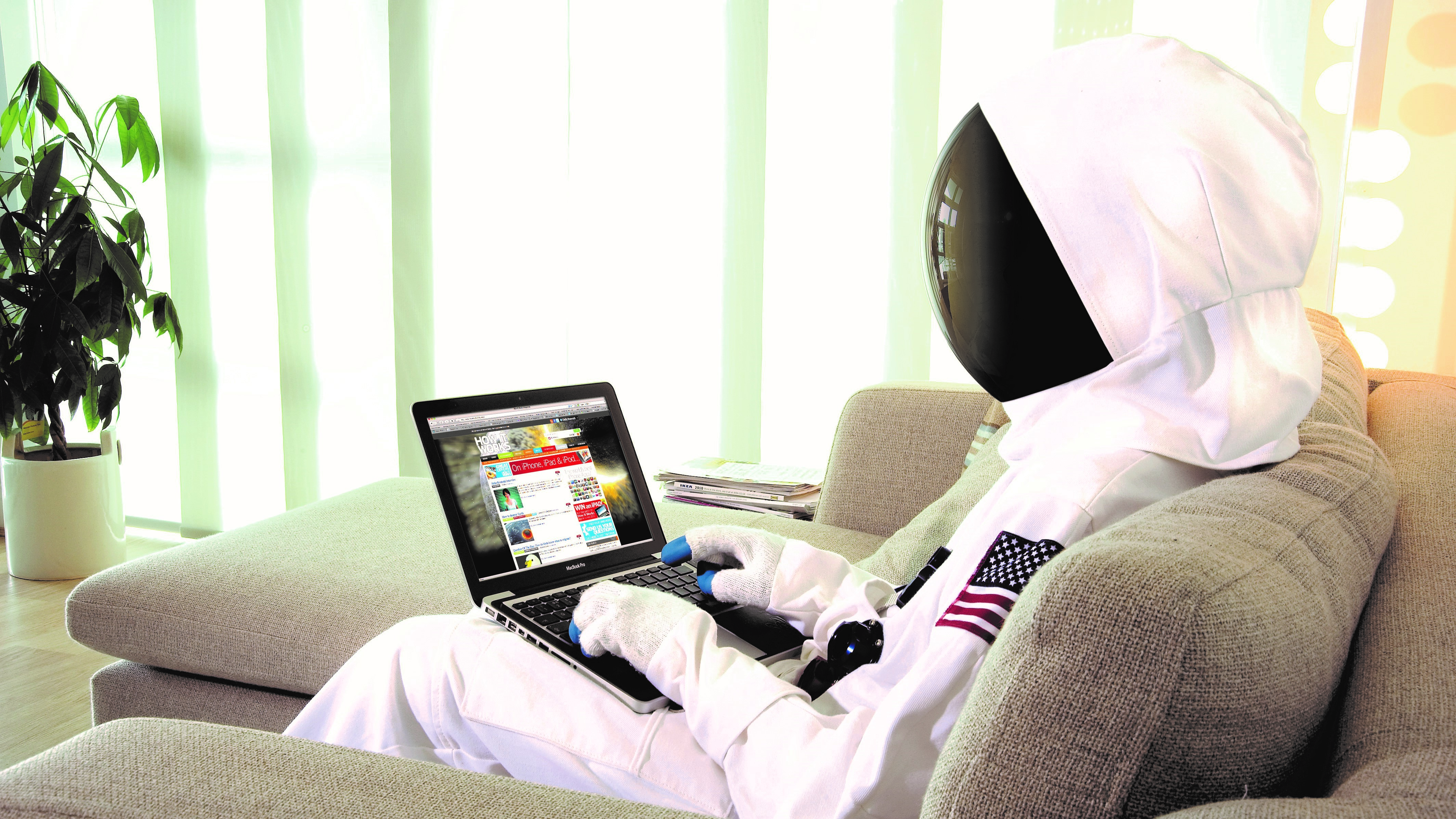 person dressed as an astronaut uses a laptop while sitting on a couch.