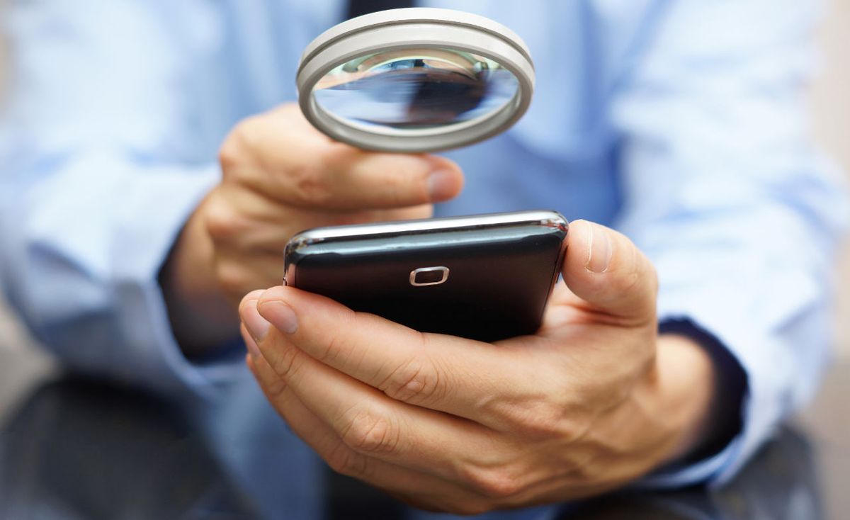 Magnifying glass is held up to cell phone. 