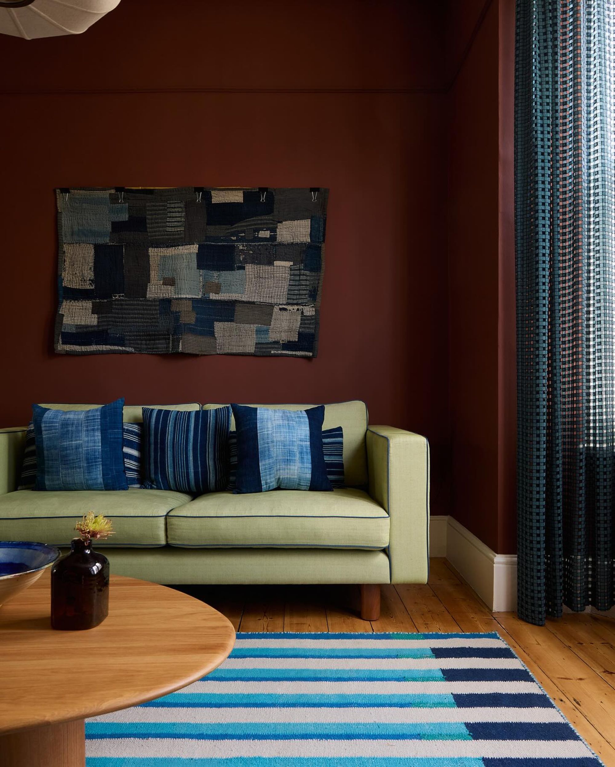 living room with a green couch, red walls, a striped blue rug, blue pillows and patchwork style artwork