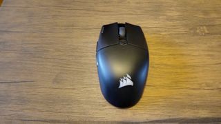 A black Corsair Katar Elite Wireless gaming mouse on a brown wooden table