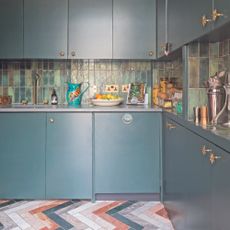 Green kitchen with slab doors, green backsplash tiles and coloured chevron flooring