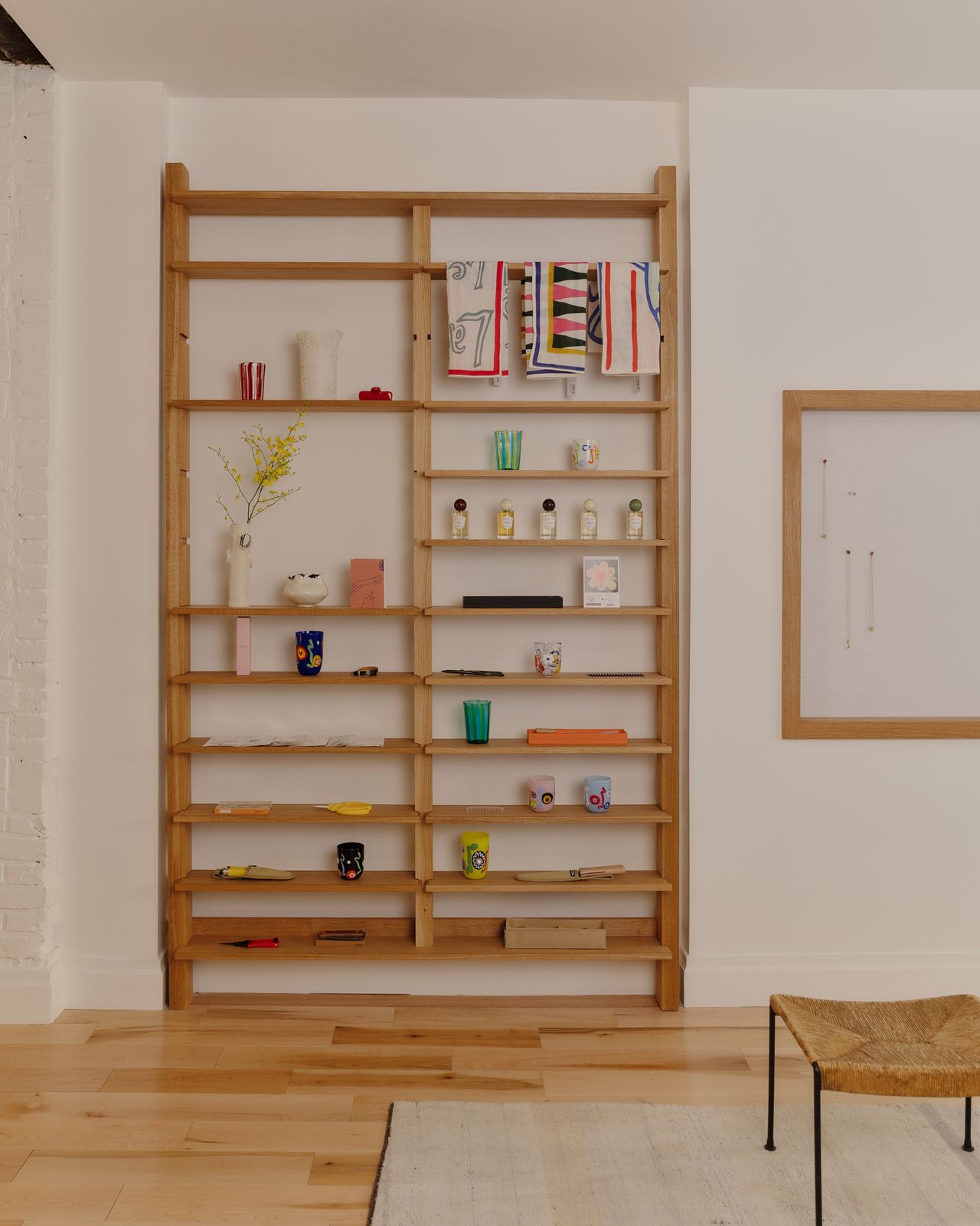 A wooden shelving unit features a series of colorful homeware accessories, including tableware and tea towels, as well as fragrance bottles.