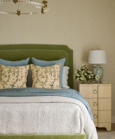 calming bedroom with neutral walls, green bed and blue throw accents with floral cushions