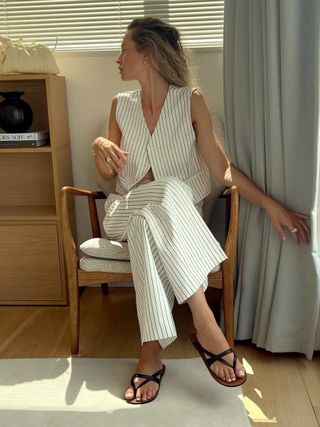 Woman sitting in chair wears striped waistcoat, trousers and strappy sandals
