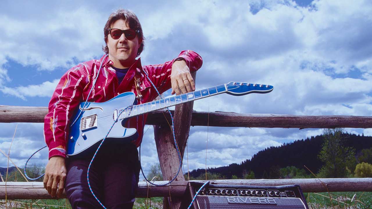 Steve Miller leaning against a fence with a guitar